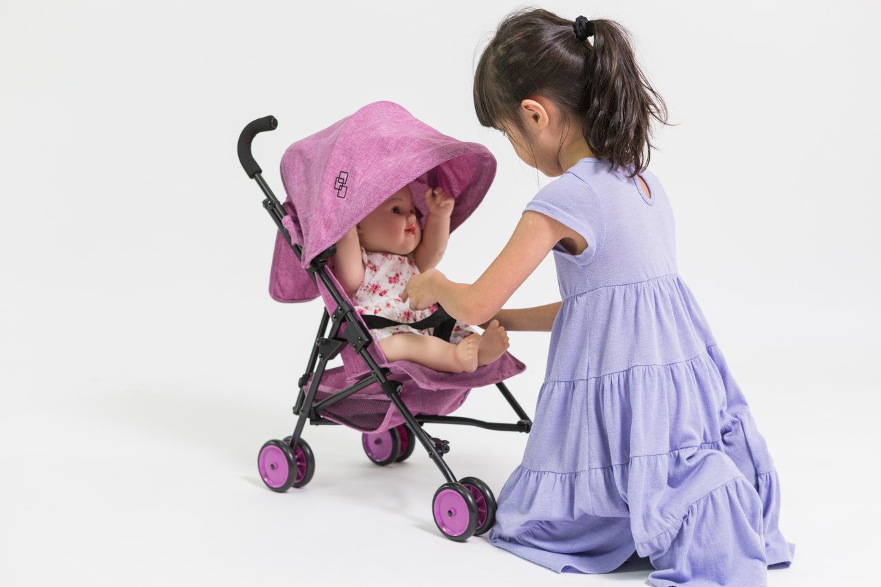 A child tucking a baby doll into a Triokid doll stroller